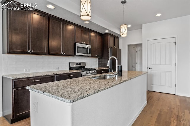 kitchen with dark brown cabinetry, light wood finished floors, decorative backsplash, appliances with stainless steel finishes, and a sink