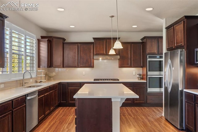 kitchen with under cabinet range hood, light countertops, appliances with stainless steel finishes, light wood-style floors, and a sink