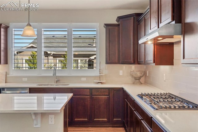 kitchen featuring stainless steel gas cooktop, a sink, decorative backsplash, under cabinet range hood, and decorative light fixtures