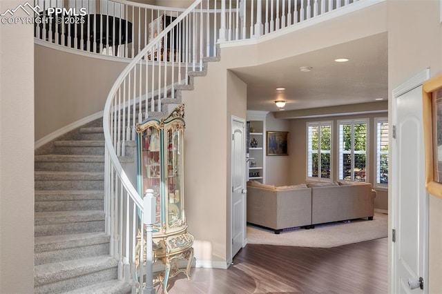 stairway with recessed lighting, a high ceiling, baseboards, and wood finished floors