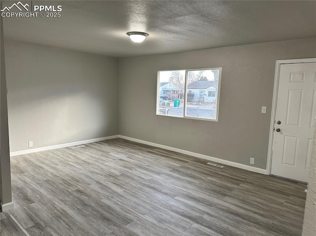 spare room featuring visible vents, a textured ceiling, baseboards, and wood finished floors