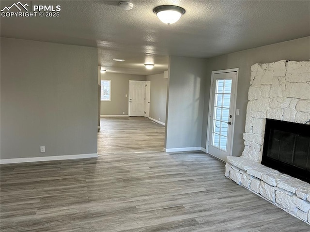 unfurnished living room featuring a textured ceiling, a fireplace, wood finished floors, and plenty of natural light