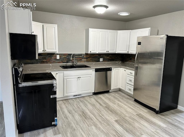 kitchen featuring stainless steel appliances, a sink, white cabinetry, light wood finished floors, and tasteful backsplash