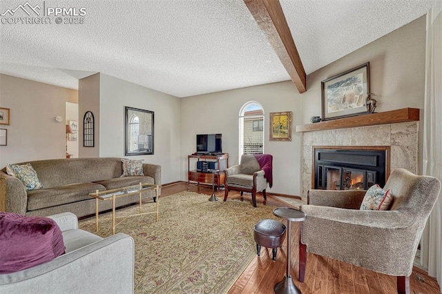 living room featuring baseboards, a tile fireplace, beamed ceiling, wood finished floors, and a textured ceiling