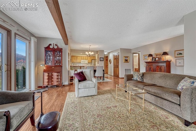 living room with a textured ceiling, light wood-type flooring, visible vents, and a notable chandelier