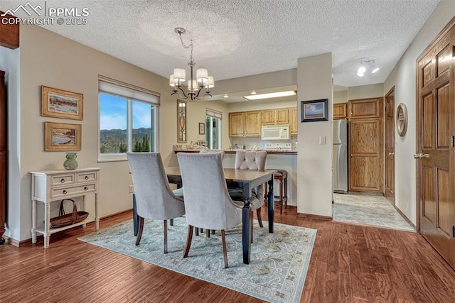 dining room featuring light wood-type flooring, a textured ceiling, baseboards, and an inviting chandelier