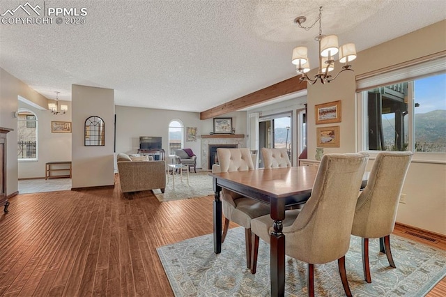 dining area featuring baseboards, wood finished floors, a textured ceiling, a fireplace, and a chandelier