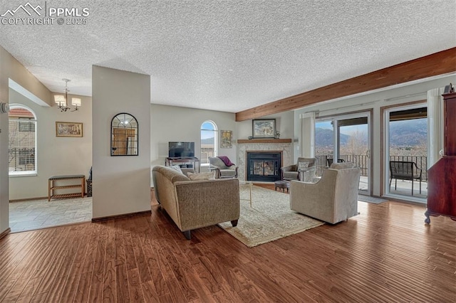 living area with baseboards, a glass covered fireplace, wood finished floors, a textured ceiling, and a chandelier