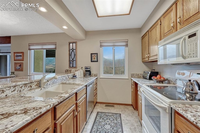 kitchen with white appliances, brown cabinetry, a sink, and baseboards