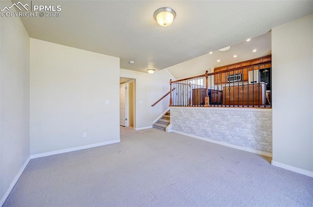 unfurnished living room with baseboards, stairway, and light colored carpet
