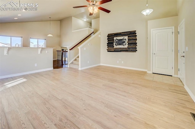 unfurnished living room featuring stairway, high vaulted ceiling, baseboards, light wood-style floors, and a ceiling fan