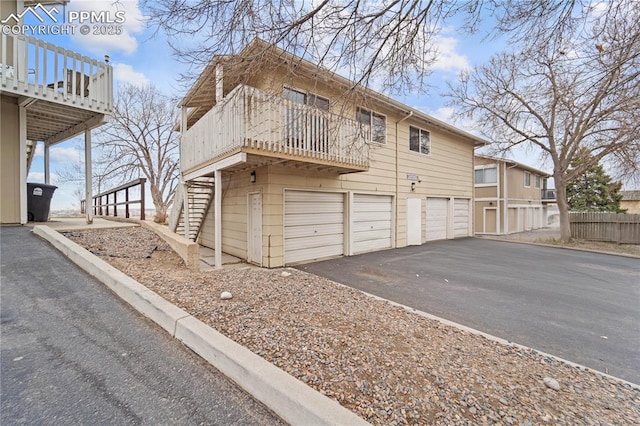 view of side of property with stairs, driveway, an attached garage, and fence