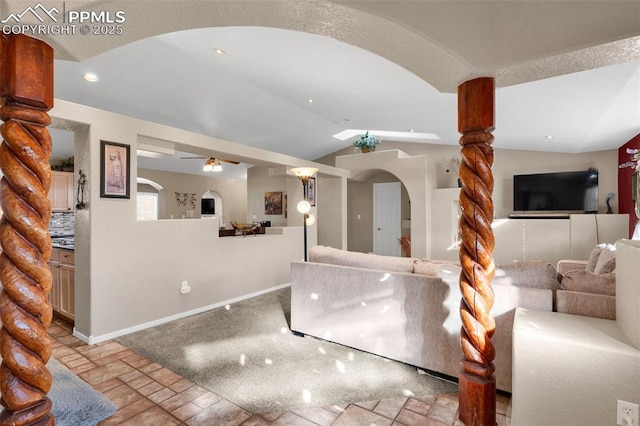 living room with a ceiling fan, arched walkways, vaulted ceiling, and baseboards