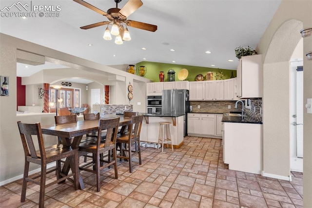 kitchen with tasteful backsplash, arched walkways, dark countertops, freestanding refrigerator, and a sink