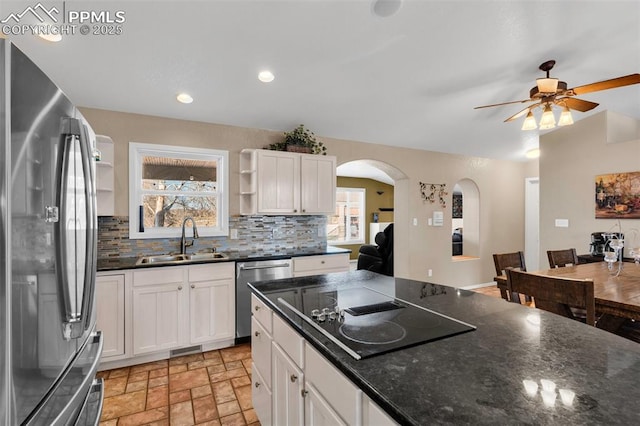 kitchen featuring arched walkways, open shelves, stainless steel appliances, stone finish floor, and a sink