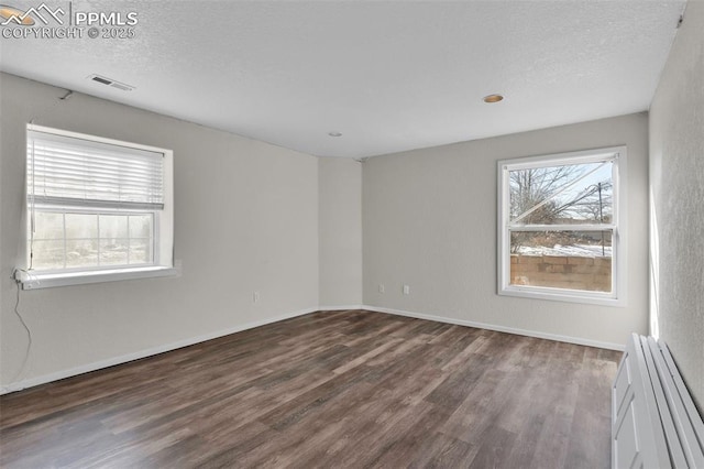 spare room featuring dark wood-style flooring, visible vents, a textured ceiling, and baseboards