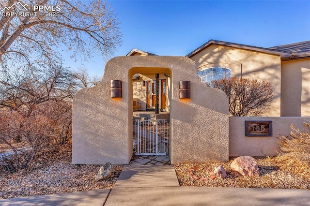 pueblo-style home with a fenced front yard, a gate, and stucco siding