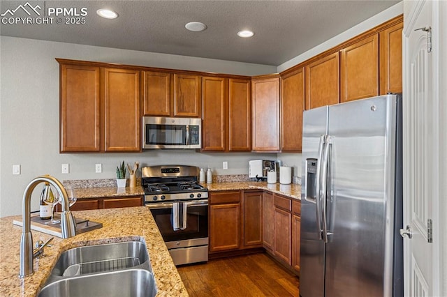 kitchen with stainless steel appliances, dark wood finished floors, brown cabinetry, and a sink