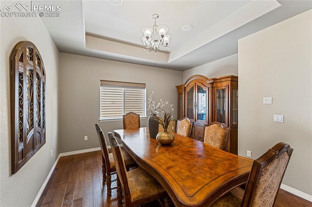 dining area with a chandelier, a tray ceiling, dark wood finished floors, and baseboards