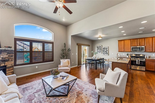 living area featuring a stone fireplace, recessed lighting, dark wood-style flooring, a ceiling fan, and baseboards