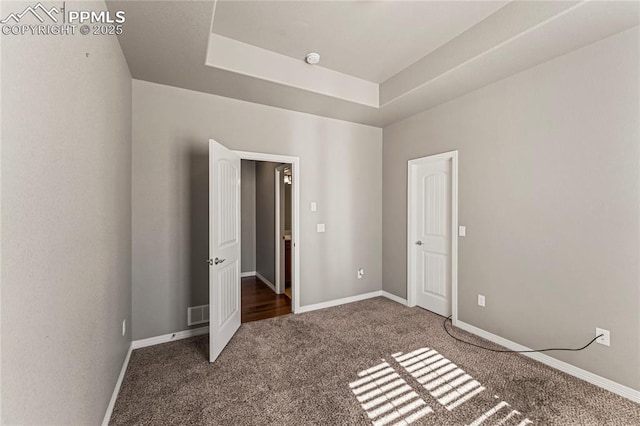 unfurnished bedroom with carpet floors, a tray ceiling, visible vents, and baseboards