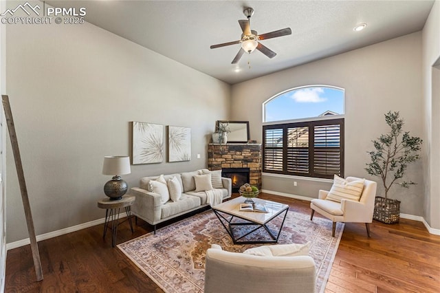 living room with a ceiling fan, a stone fireplace, baseboards, and hardwood / wood-style flooring