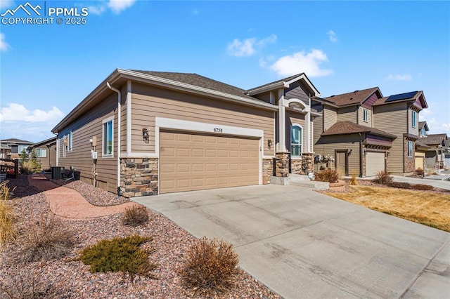 view of front of property featuring central AC unit, concrete driveway, stone siding, a residential view, and an attached garage