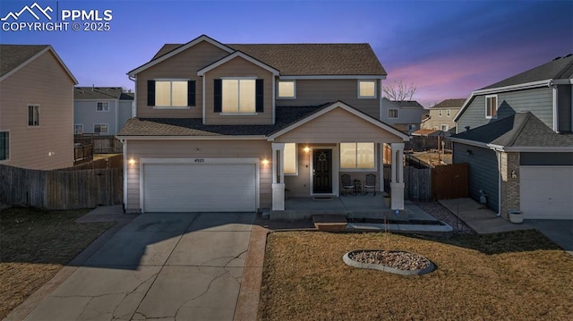 traditional-style home featuring driveway, a shingled roof, an attached garage, and fence