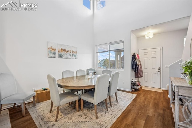 dining area with dark wood-type flooring, a high ceiling, and baseboards