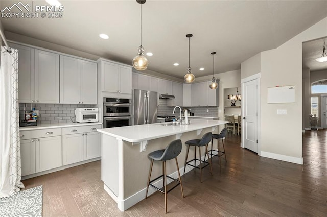 kitchen with tasteful backsplash, dark wood-style flooring, stainless steel appliances, light countertops, and a sink