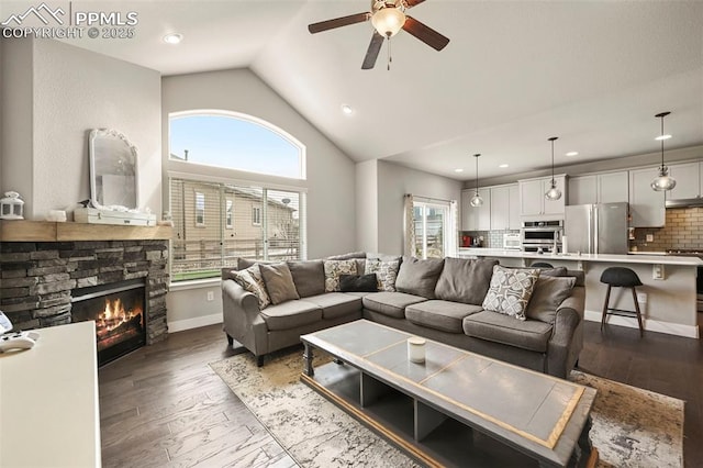 living room with baseboards, a ceiling fan, wood finished floors, a fireplace, and high vaulted ceiling