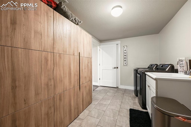 laundry area featuring a textured ceiling, light tile patterned floors, baseboards, washer and dryer, and cabinet space