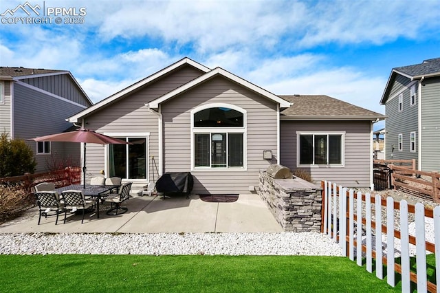 back of property with a shingled roof, an outdoor kitchen, a fenced backyard, a yard, and a patio area