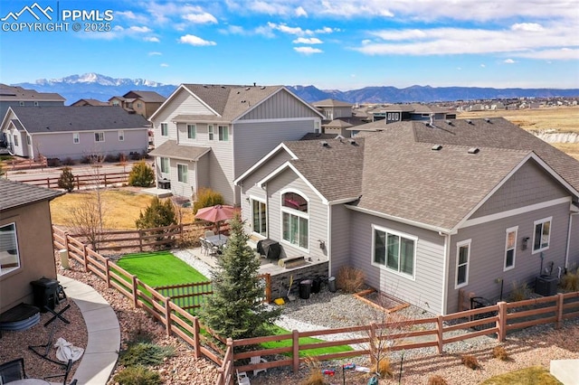 rear view of house with a patio, a fenced backyard, a mountain view, roof with shingles, and a residential view