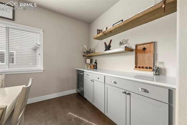 bar with beverage cooler, a bar, dark wood finished floors, and baseboards