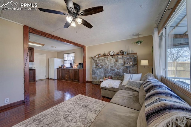 living area featuring dark wood finished floors, a textured ceiling, baseboards, and ceiling fan