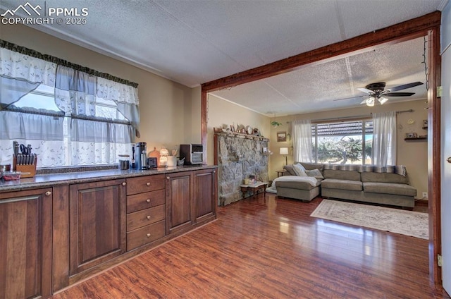 kitchen with a textured ceiling, wood finished floors, a ceiling fan, open floor plan, and beamed ceiling