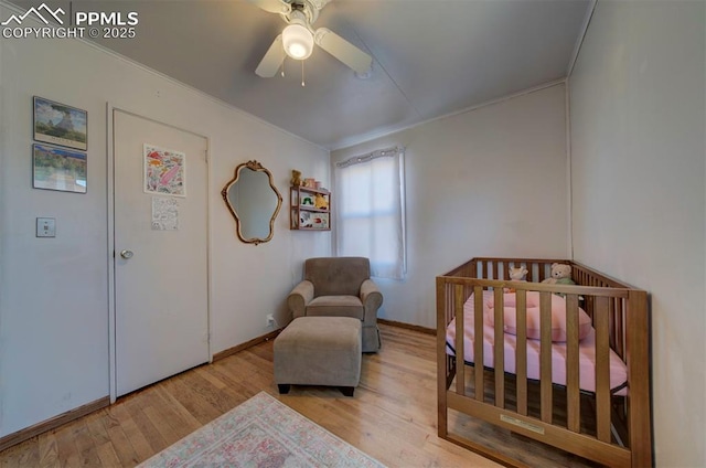 bedroom with a nursery area, ceiling fan, wood finished floors, and baseboards