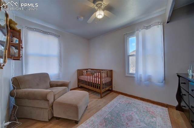 bedroom featuring a crib, light wood-style flooring, baseboards, and ceiling fan