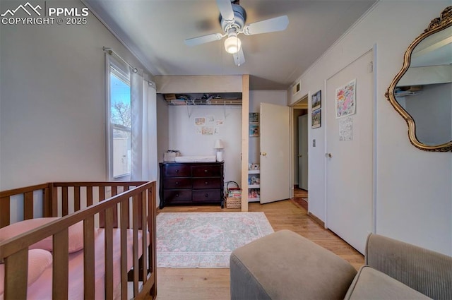 bedroom featuring ceiling fan, a crib, visible vents, and light wood-style floors