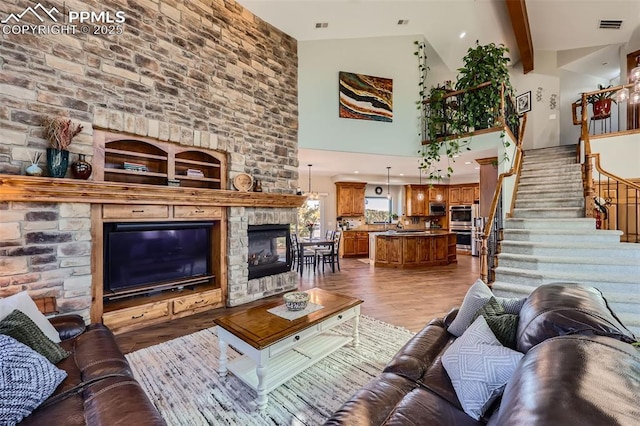 living area featuring beam ceiling, visible vents, light wood-style flooring, stairway, and a stone fireplace