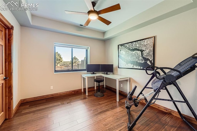 office space featuring a tray ceiling, visible vents, ceiling fan, wood finished floors, and baseboards