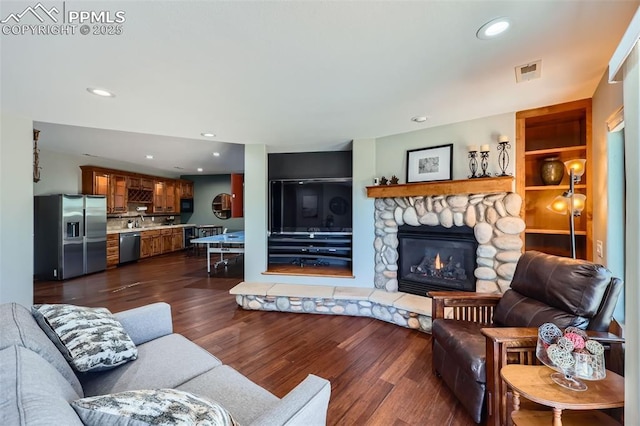 living area with recessed lighting, visible vents, dark wood-type flooring, and a stone fireplace