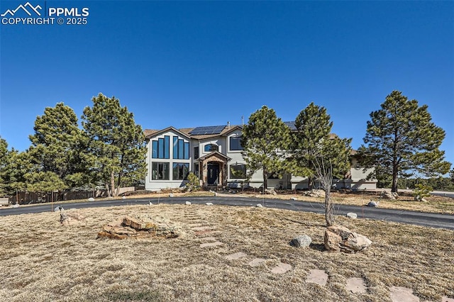 view of front of property featuring solar panels, fence, and stucco siding