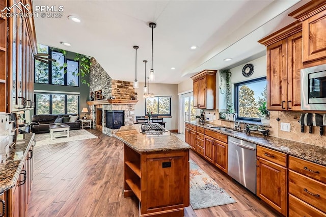 kitchen featuring a fireplace, stainless steel appliances, tasteful backsplash, a sink, and dark stone counters