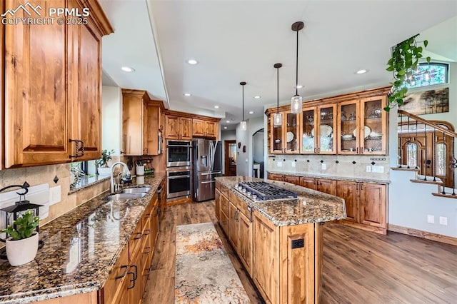 kitchen with arched walkways, stainless steel appliances, brown cabinetry, a sink, and a kitchen island