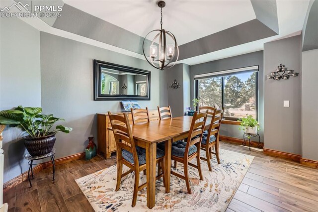 dining room with baseboards, a raised ceiling, light wood-style flooring, and an inviting chandelier