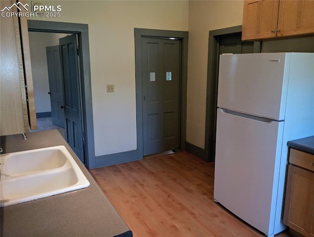 kitchen with freestanding refrigerator, a sink, light wood-style flooring, and baseboards