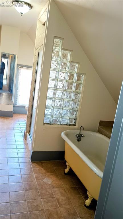 bathroom featuring lofted ceiling, a freestanding tub, and tile patterned flooring