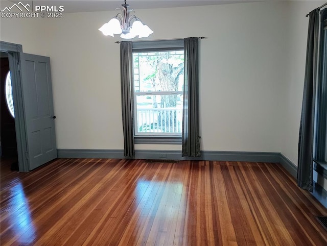 spare room with baseboards, hardwood / wood-style floors, and a notable chandelier